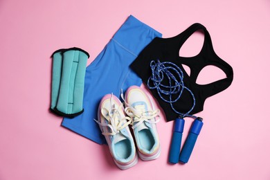 Photo of Sportswear, ankle weights, skipping rope and sneakers on pink background, flat lay