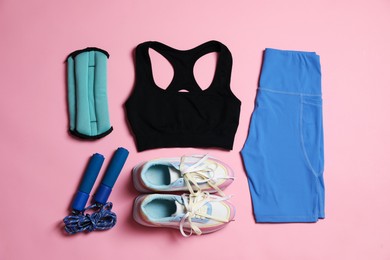 Photo of Sportswear, ankle weights, skipping rope and sneakers on pink background, flat lay