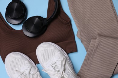 Photo of Sportswear, headphones and sneakers on light blue background, flat lay
