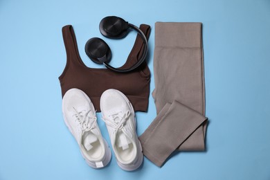 Photo of Sportswear, headphones and sneakers on light blue background, flat lay