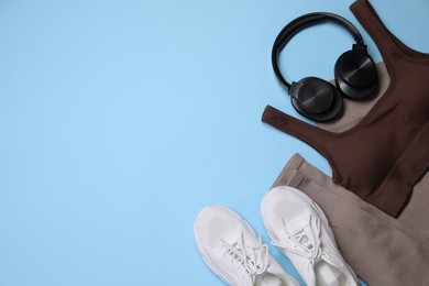 Photo of Sportswear, headphones and sneakers on light blue background, flat lay. Space for text