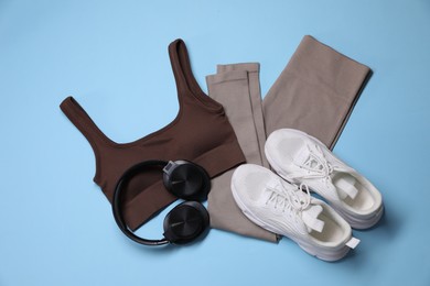 Photo of Sportswear, headphones and sneakers on light blue background, flat lay
