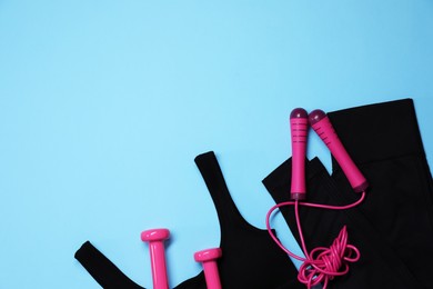 Photo of Sportswear, skipping rope and dumbbells on light blue background, flat lay. Space for text