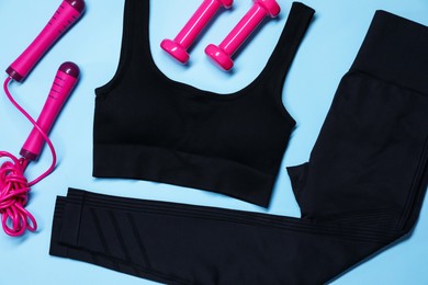 Photo of Sportswear, skipping rope and dumbbells on light blue background, flat lay