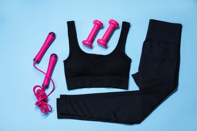 Photo of Sportswear, skipping rope and dumbbells on light blue background, flat lay