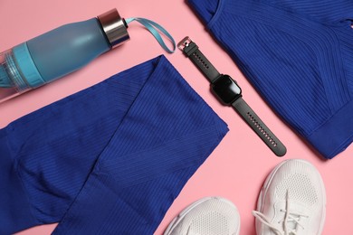 Photo of Sportswear, watch, bottle of water and sneakers on pink background, flat lay