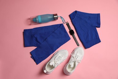 Photo of Sportswear, watch, bottle of water and sneakers on pink background, flat lay