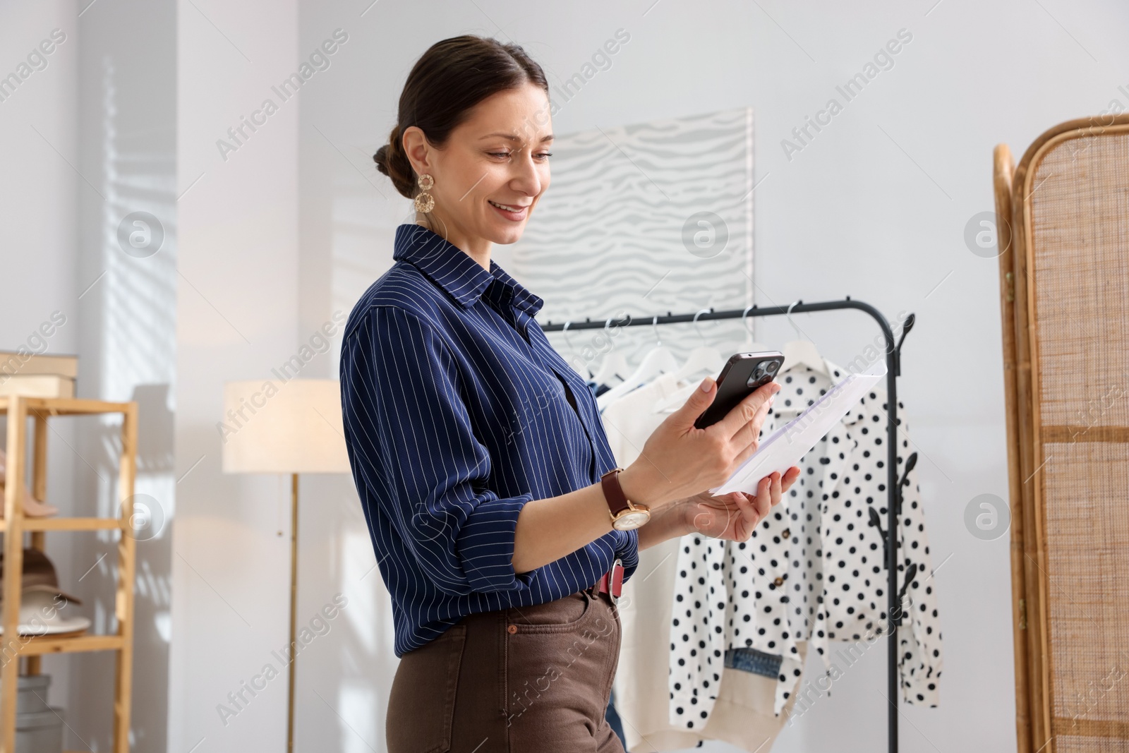 Photo of Professional stylist with smartphone and picture of outfit working indoors