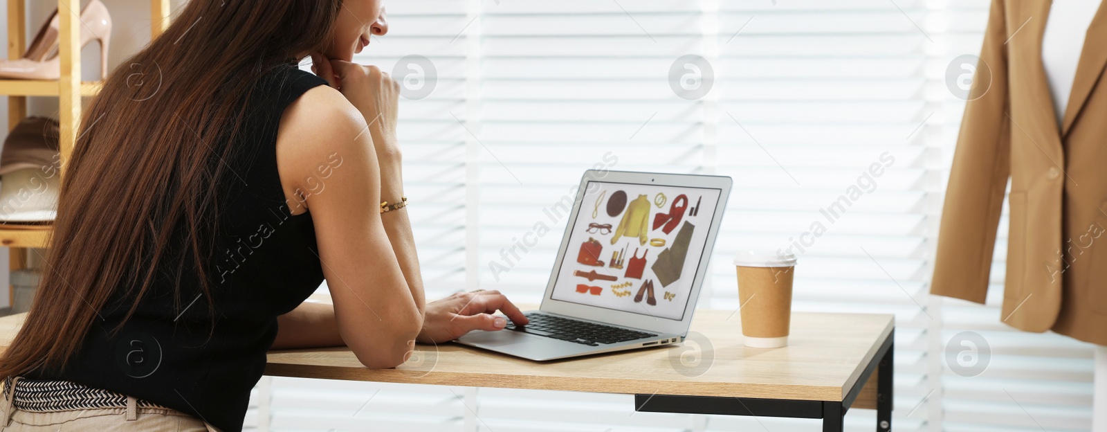 Photo of Professional stylist making collage with outfit on laptop at desk indoors