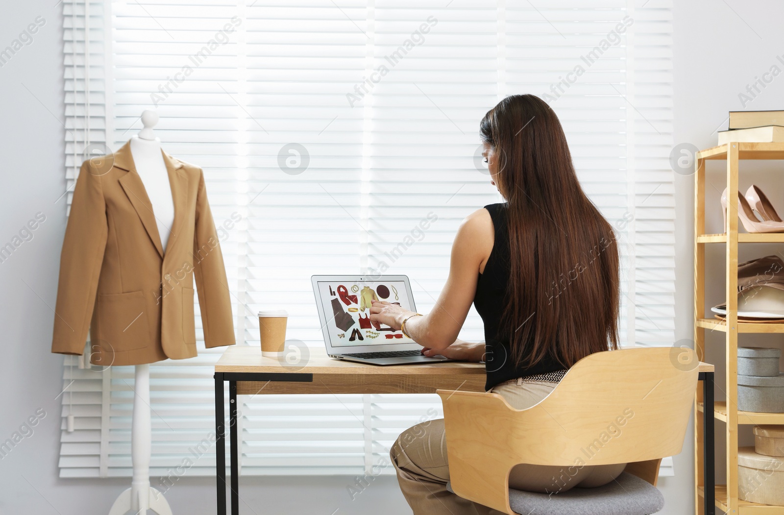 Professional stylist making collage with outfit on laptop at desk indoors Photo of Professional stylist making collage with outfit on laptop at desk indoors