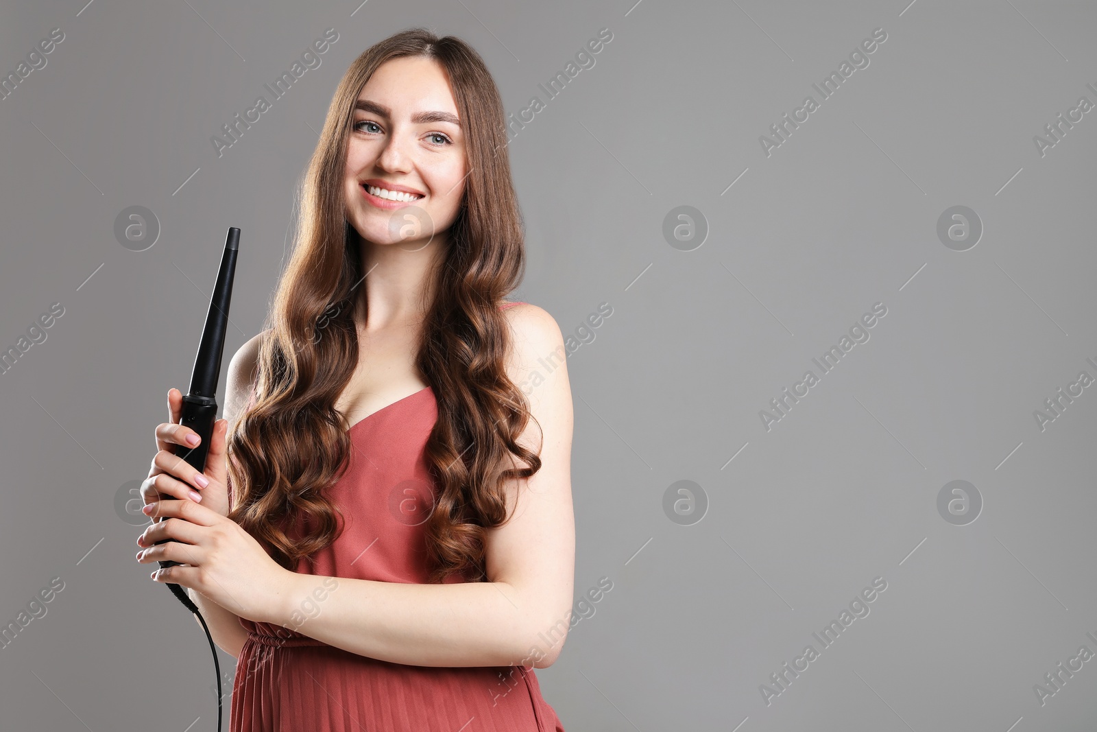 Woman with beautiful hairstyle and curling iron on grey background. Space for text Photo of Woman with beautiful hairstyle and curling iron on grey background. Space for text