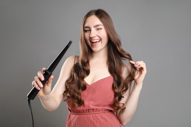Photo of Woman with beautiful hairstyle and curling iron on grey background