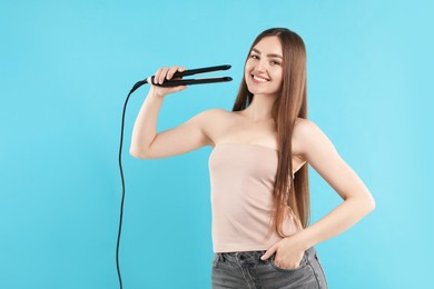 Photo of Hairdresser straightening woman's hair on light blue background