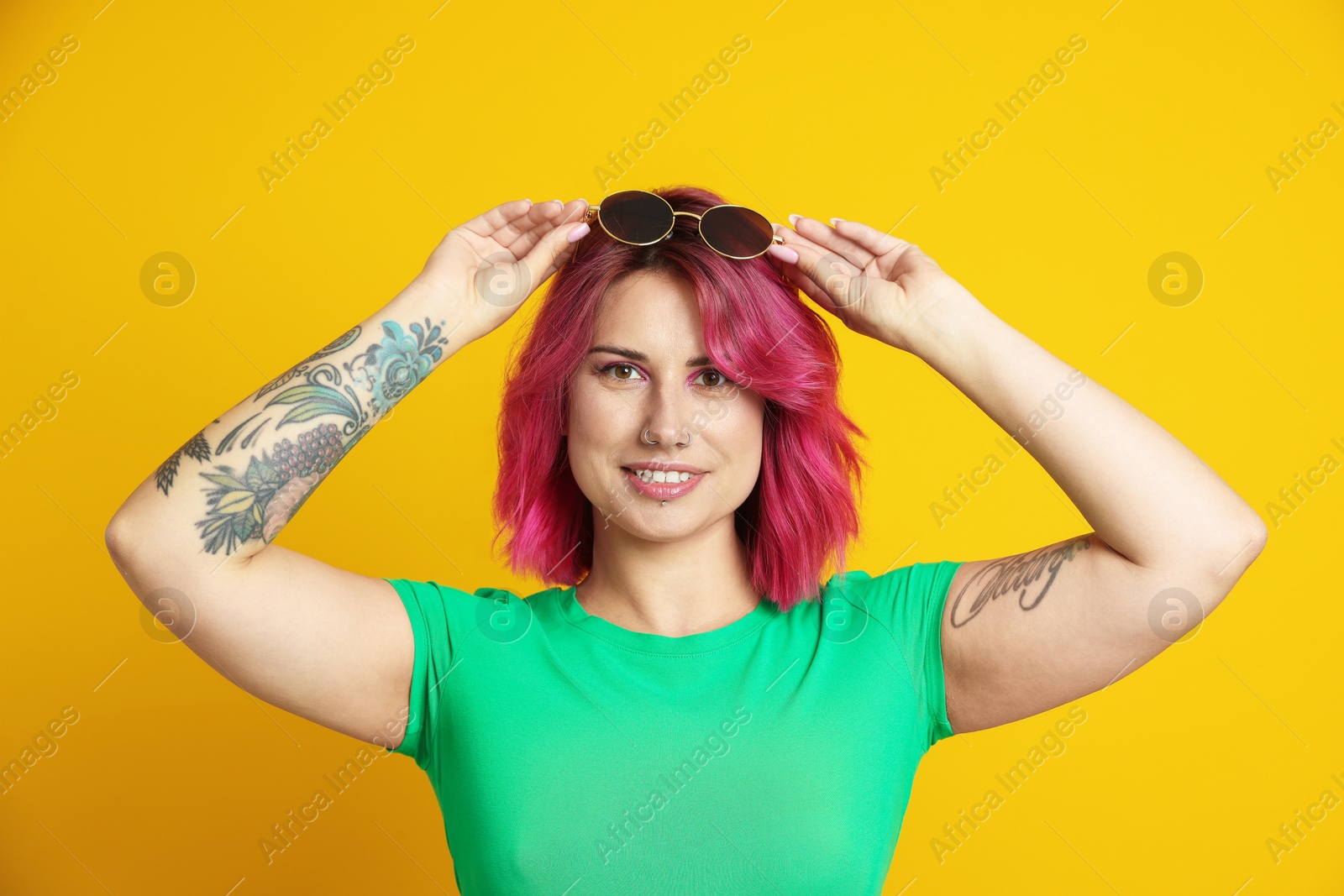 Beautiful woman with pink dyed hair and sunglasses on yellow background Photo of Beautiful woman with pink dyed hair and sunglasses on yellow background
