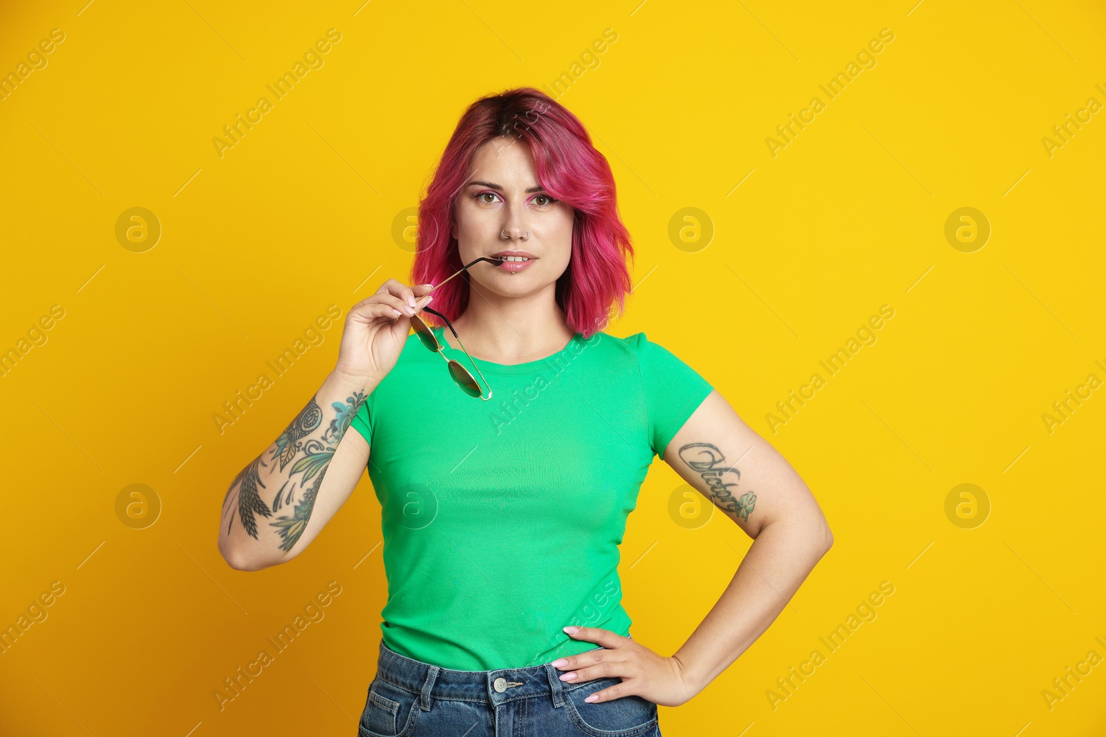 Beautiful woman with pink dyed hair and sunglasses on yellow background Photo of Beautiful woman with pink dyed hair and sunglasses on yellow background