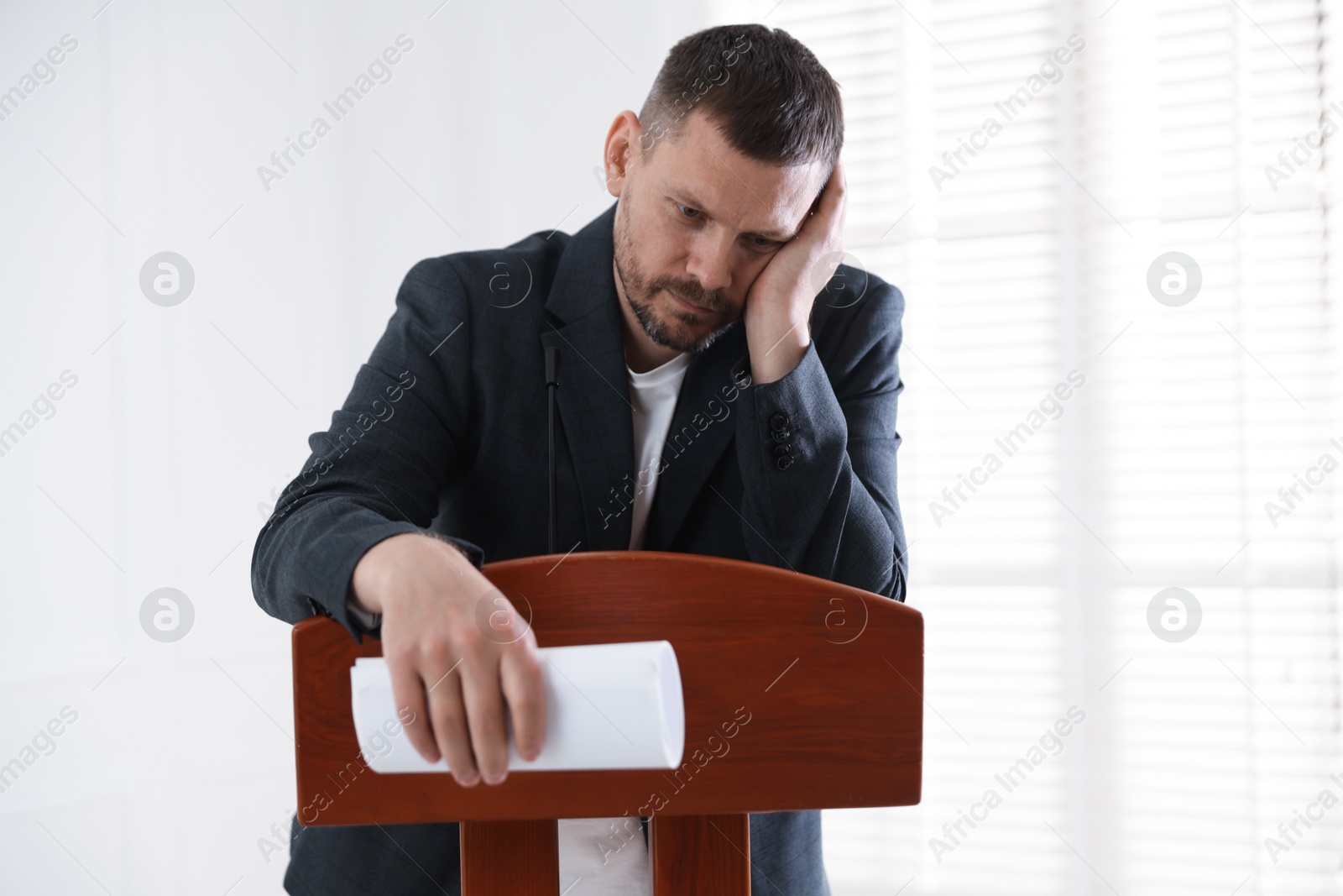 Fear of public speaking. Nervous man with microphone at lectern indoors Photo of Fear of public speaking. Nervous man with microphone at lectern indoors
