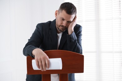 Photo of Fear of public speaking. Nervous man with microphone at lectern indoors