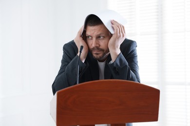 Photo of Fear of public speaking. Nervous man with microphone at lectern indoors
