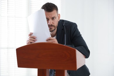 Photo of Fear of public speaking. Nervous man with microphone at lectern indoors