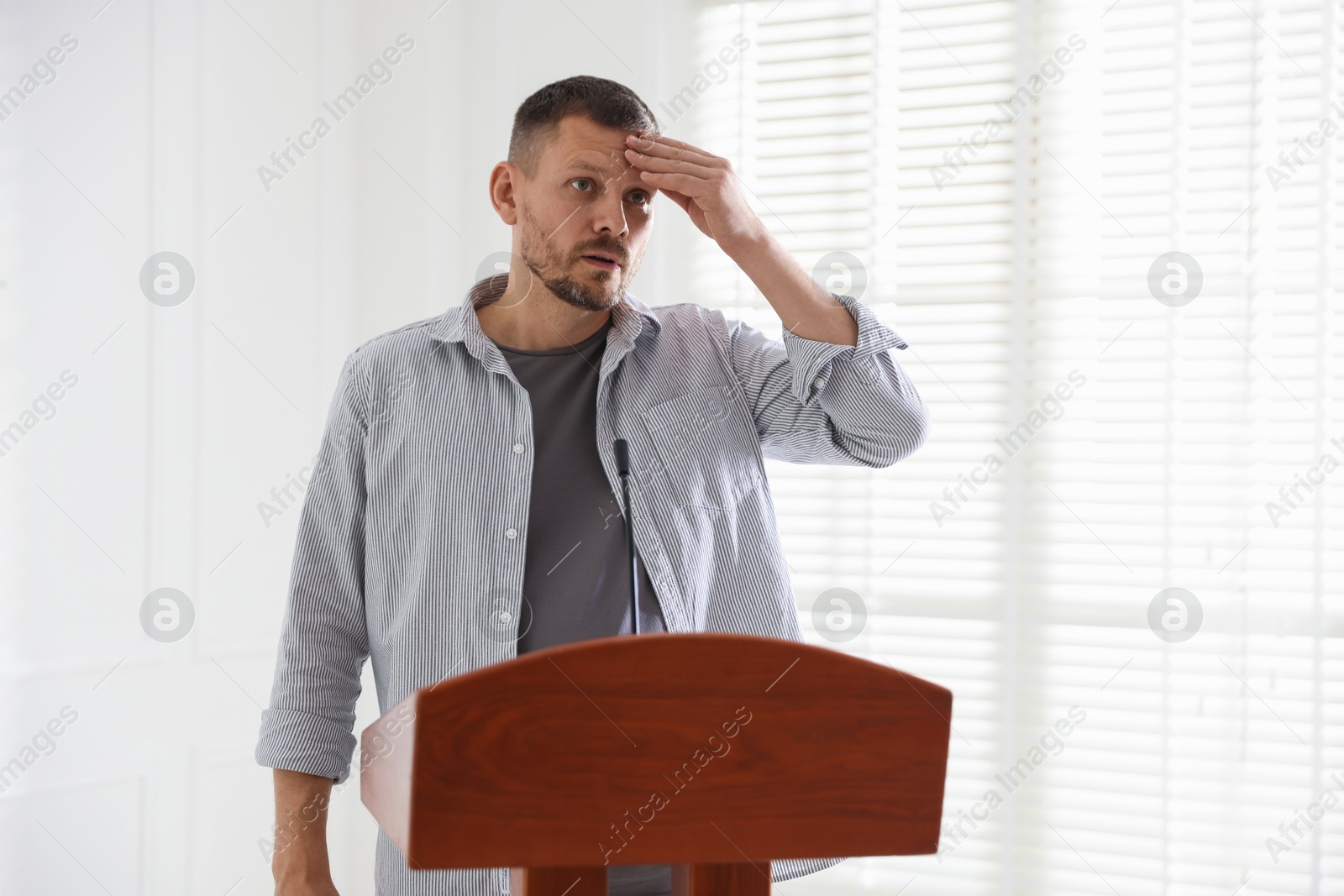 Fear of public speaking. Nervous man with microphone at lectern indoors Photo of Fear of public speaking. Nervous man with microphone at lectern indoors