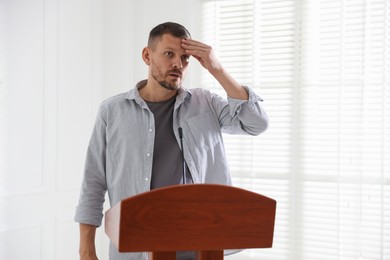 Photo of Fear of public speaking. Nervous man with microphone at lectern indoors