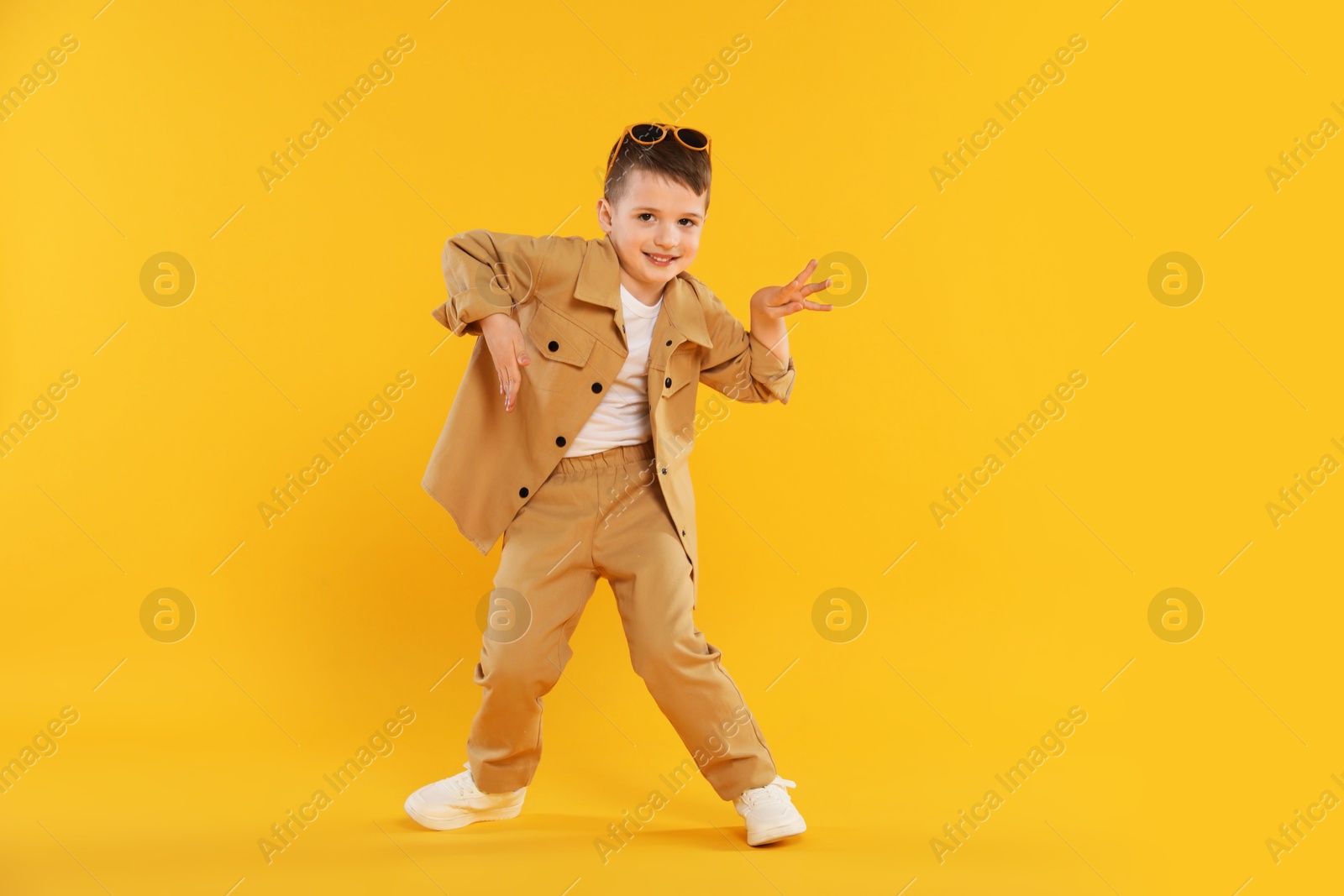 Happy little boy in sunglasses dancing on orange background Photo of Happy little boy in sunglasses dancing on orange background