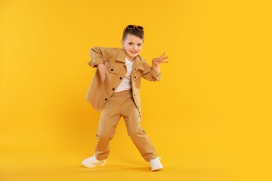 Photo of Happy little boy in sunglasses dancing on orange background
