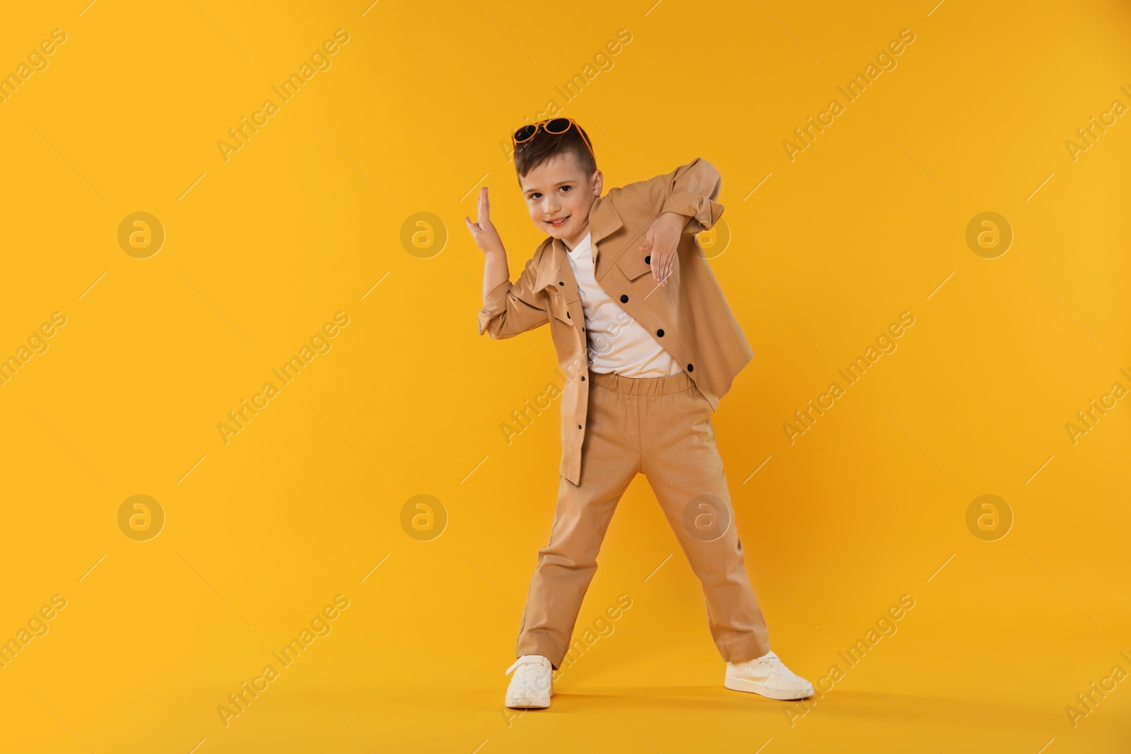 Happy little boy in sunglasses dancing on orange background. Space for text Photo of Happy little boy in sunglasses dancing on orange background. Space for text