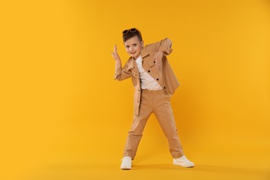 Photo of Happy little boy in sunglasses dancing on orange background. Space for text