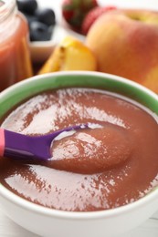 Photo of Baby food. Eating tasty puree with spoon at white table, closeup