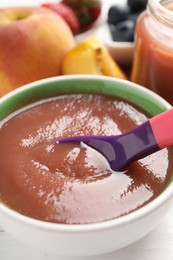 Photo of Baby food. Eating tasty puree with spoon at white wooden table, closeup