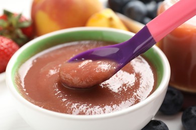 Photo of Baby food. Eating tasty puree with spoon at white table, closeup
