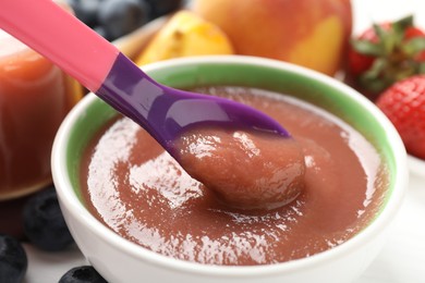 Photo of Baby food. Eating tasty puree with spoon at white table, closeup