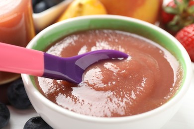 Photo of Baby food. Eating tasty puree with spoon at white table, closeup