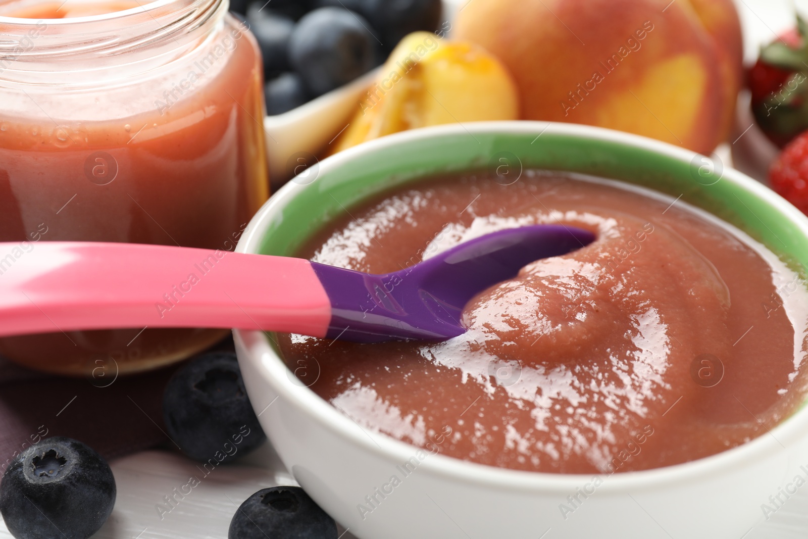 Baby food. Eating tasty puree with spoon at white wooden table, closeup Photo of Baby food. Eating tasty puree with spoon at white wooden table, closeup