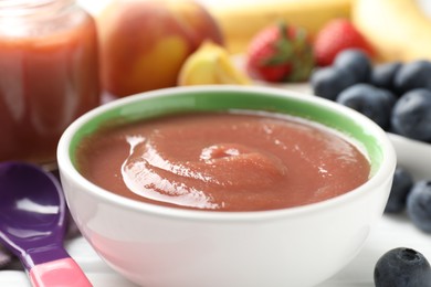 Photo of Baby food. Tasty puree in bowl, spoon and ingredients on white table, closeup