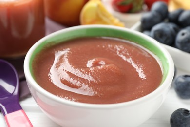 Photo of Baby food. Tasty puree in bowl, spoon and ingredients on white table, closeup