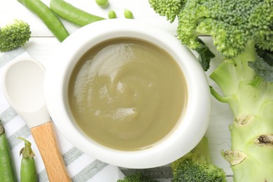 Photo of Baby food. Tasty puree in bowl, spoon and ingredients on white wooden table, flat lay