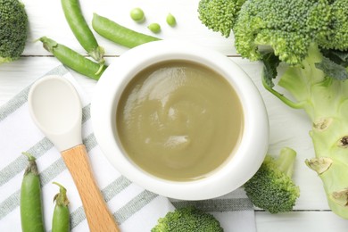 Photo of Baby food. Tasty puree in bowl, spoon and ingredients on white wooden table, flat lay