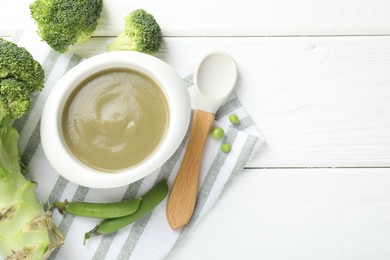 Photo of Baby food. Tasty puree in bowl, spoon and ingredients on white wooden table, flat lay. Space for text