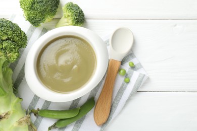 Photo of Baby food. Tasty puree in bowl, spoon and ingredients on white wooden table, flat lay. Space for text
