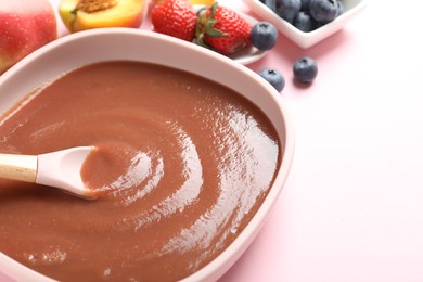 Photo of Baby food. Eating tasty puree with spoon at pink table, closeup