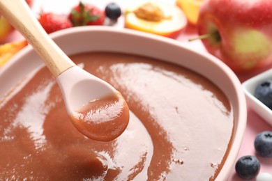 Photo of Baby food. Eating tasty puree with spoon at pink table, closeup