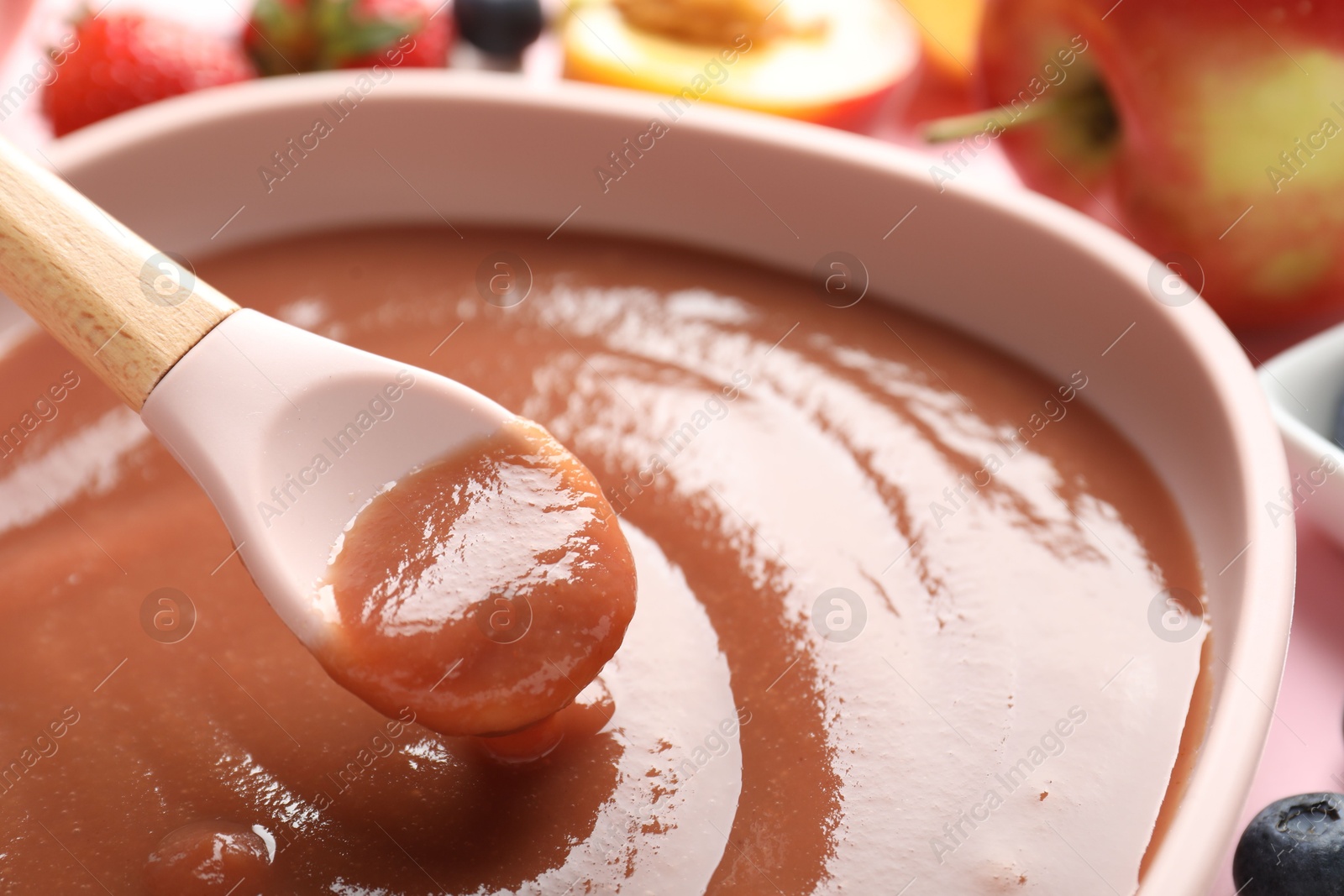 Baby food. Eating tasty puree with spoon at pink table, closeup Photo of Baby food. Eating tasty puree with spoon at pink table, closeup