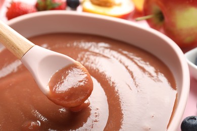 Photo of Baby food. Eating tasty puree with spoon at pink table, closeup