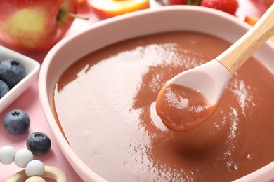 Photo of Baby food. Eating tasty puree with spoon at pink table, closeup