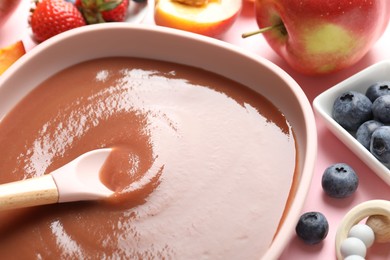 Photo of Baby food. Eating tasty puree with spoon at pink table, closeup