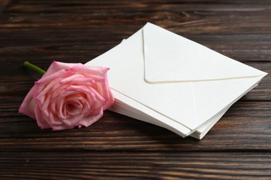 Photo of Stack of love letters and beautiful rose on wooden table, closeup