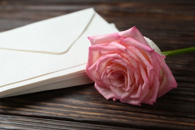 Photo of Stack of love letters and beautiful rose on wooden table, closeup