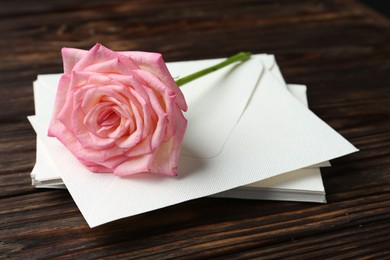 Photo of Stack of love letters and beautiful rose on wooden table, closeup